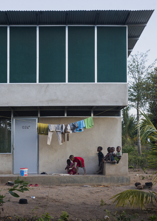 Children are playing in front of a two-storey building with washing hanging on a clothesline.