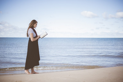 Læsende kvinde i sommertøj ved havkant