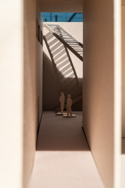 View of into a sketch model of the entrance pathway, with two small figures and a stair creating a shadow