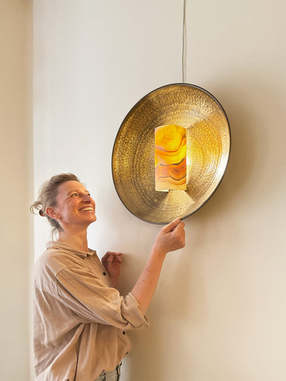 A person examines a wall-mounted lamp with a golden shade.
