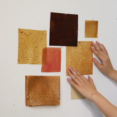 Material samples in warm tones attached to a wall, with hands visible in the frame.