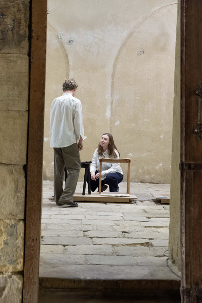 Two people interacting beside stools in a stone interior
