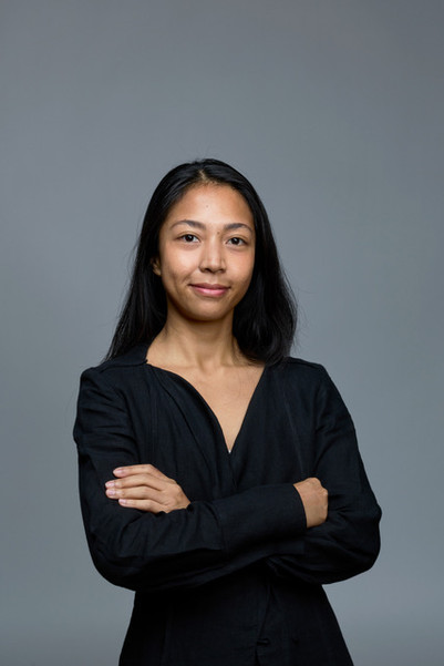 Portrait of a woman in black with folded arms against a gray background.