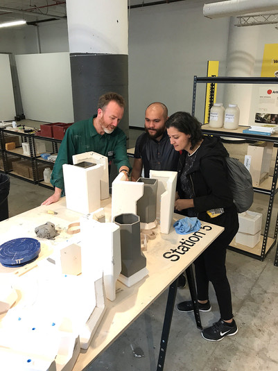 Three people examine ceramic forms together in a workshop.