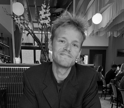Black-and-white portrait of a smiling man seated in a restaurant.