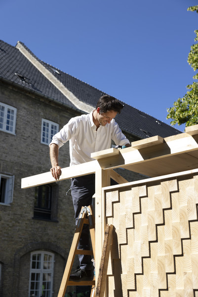 Man on a ladder works on the roof of a wooden structure.