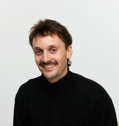 Portrait of a smiling man with a mustache wearing a black turtleneck.