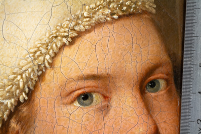 Detail of a cracked painting showing two blue-grey eyes and a ruler along the right edge.