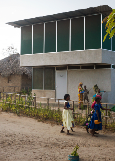 Women and children outside a modern two-storey building with green facade panels.