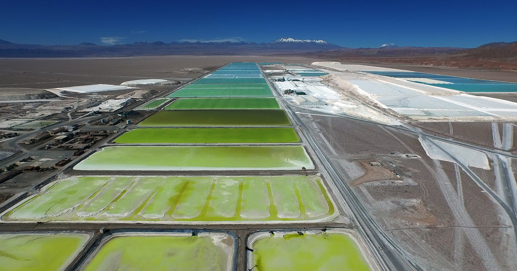 Colored evaporation ponds for lithium extraction in a dry desert landscape with mountains in the background.