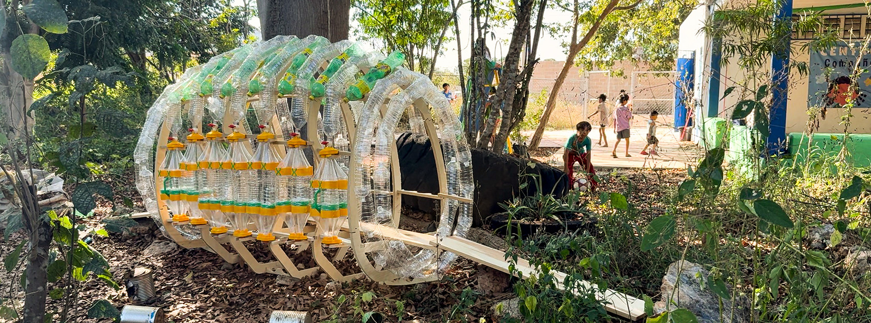 Tunnel-like structure made from recycled plastic bottles in a green outdoor area.