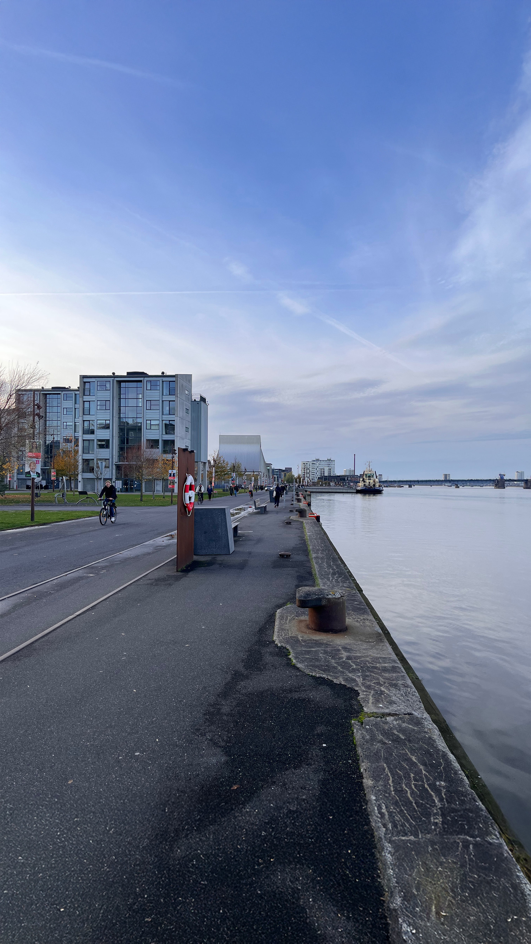 Waterfront path with cyclists, modern buildings, and calm water.