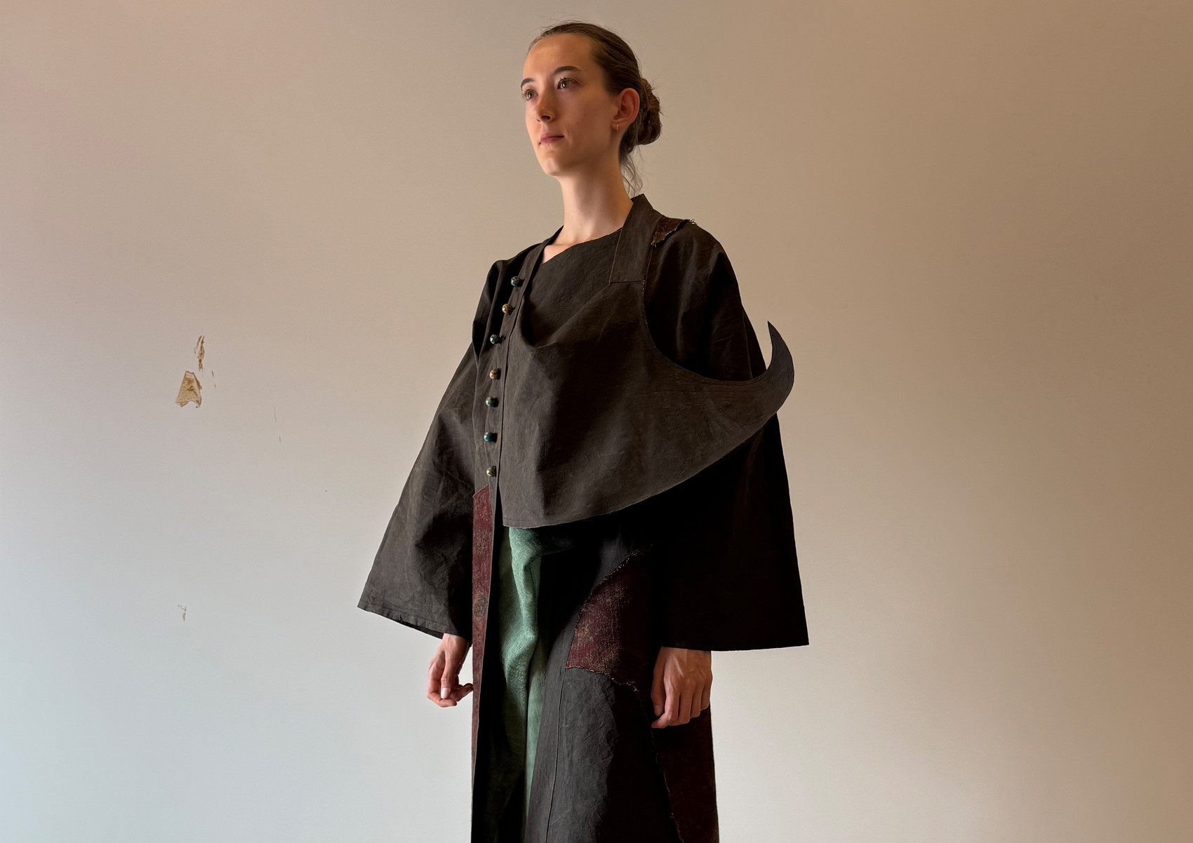 Model wearing a dark layered garment inspired by a moving temple, with an extended eave-like structure and faded textile surfaces suggesting incense smoke, time, wind, and rain.