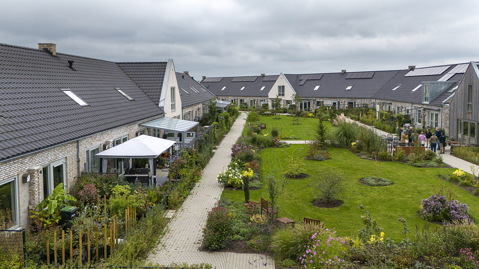 Housing area with row houses around a shared green courtyard with paths, planting, and seating areas