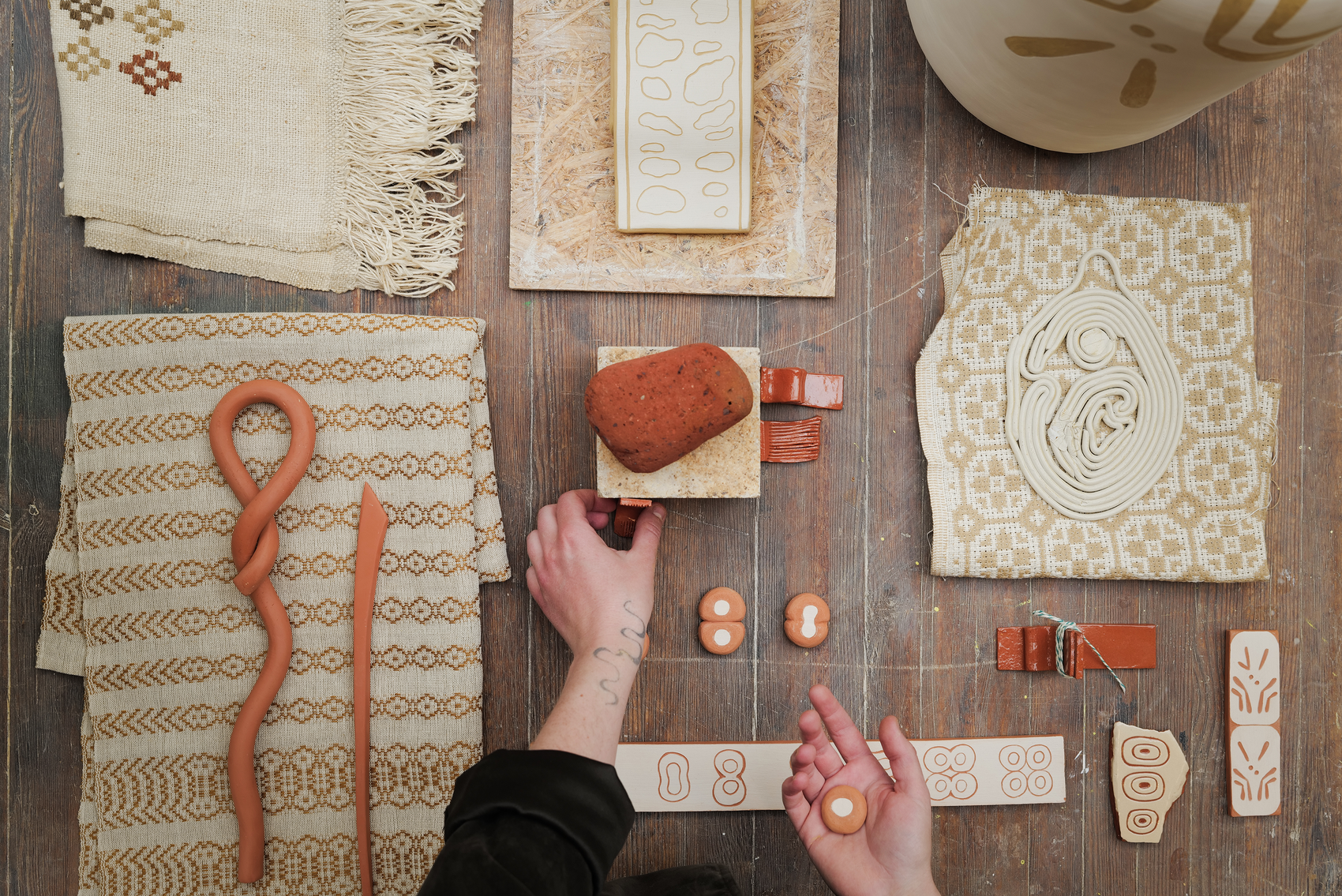 Hands arranging clay samples and tools on a worktable.
